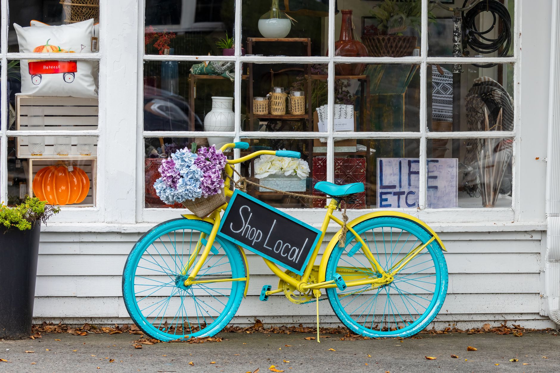 A colorful bicycle with flowers and 'Shop Local' sign outside a store in Sudbury, MA.