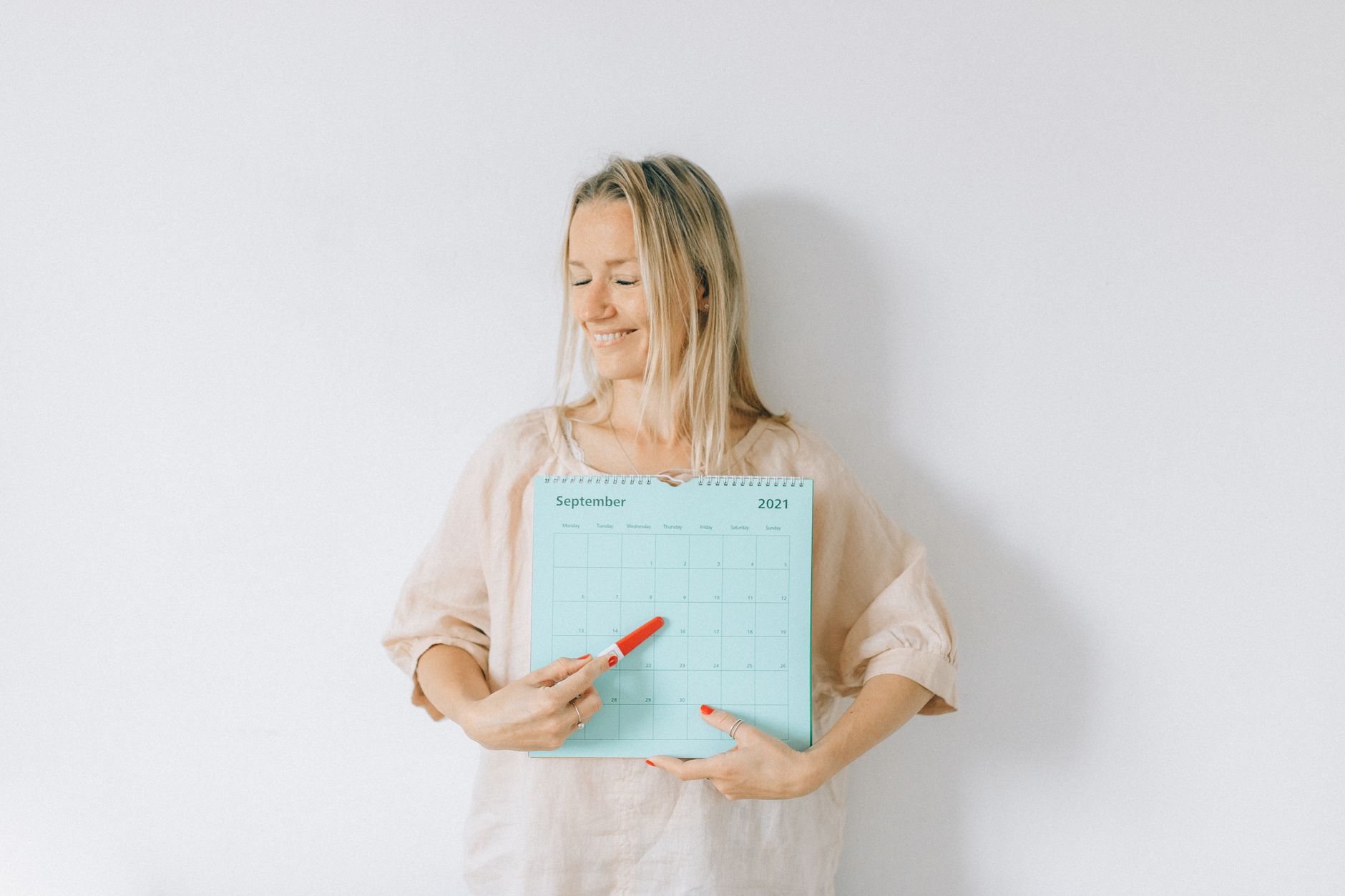 Smiling woman points at a date on a calendar, conveying excitement and anticipation.