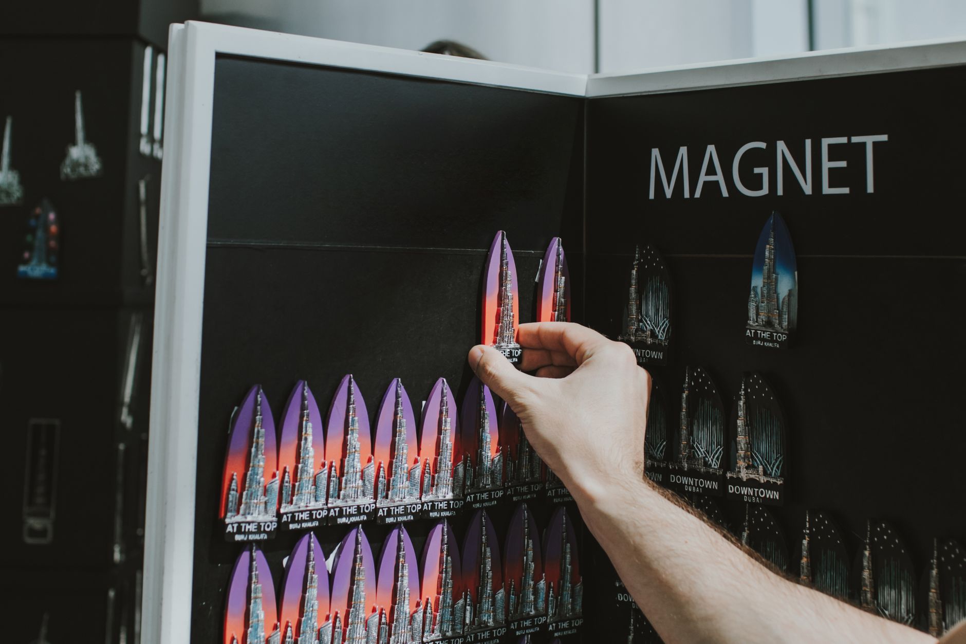 A hand selecting colorful Burj Khalifa souvenir magnets from a display in Dubai shop.