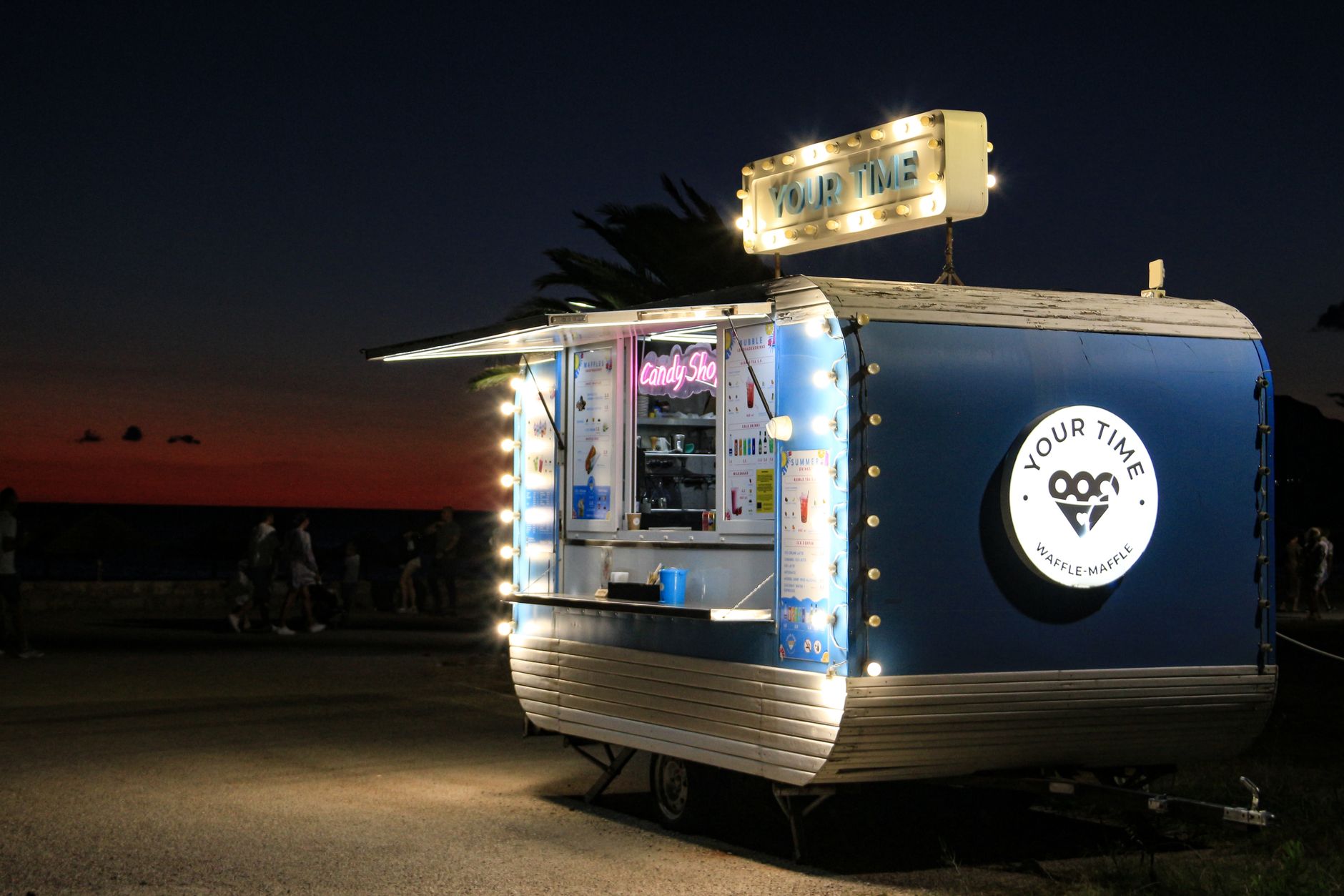 A vibrant food truck lit with neon signs at dusk in Bar, Montenegro.